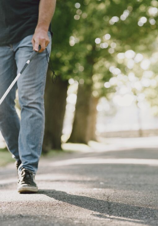 Man met blindegeleidestok wandelend in park.